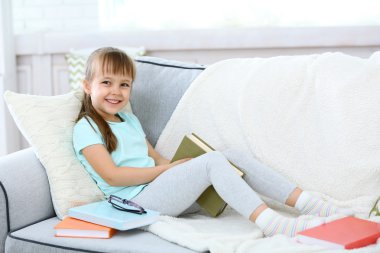 Kitap ile kanepede oturan küçük kız