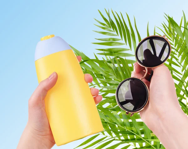 Fles van zonnebrand crème en zonnebril in handen — Stockfoto