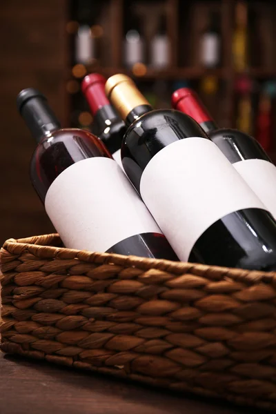 Wattled basket with labeled bottles of wine on unfocused dark background