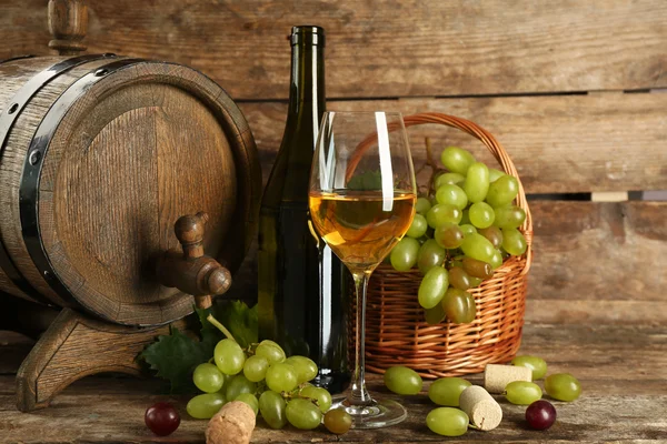 Uva branca e vermelha com garrafa de vinho perto do barril no fundo de madeira — Fotografia de Stock