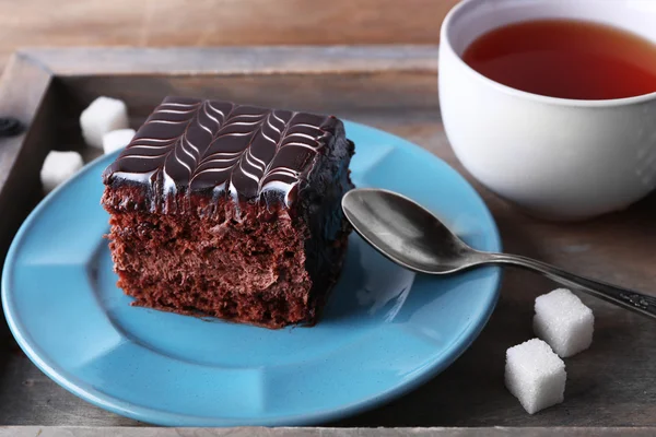 Sweet chocolate cake on blue plate with cup of tea on wooden tray — Stock Photo, Image