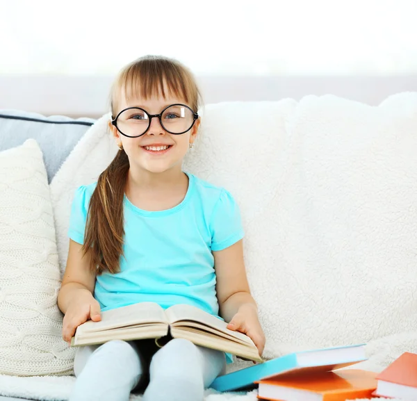 Bambina seduta sul divano con libro — Foto Stock