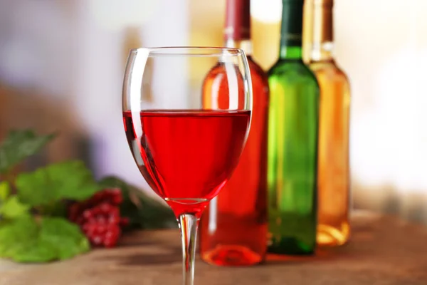 Copa de vino tinto con botellas de colores sobre mesa de madera sobre fondo desenfocado — Foto de Stock