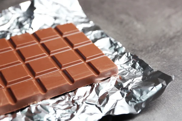 Barra de chocolate en papel de aluminio sobre fondo gris —  Fotos de Stock