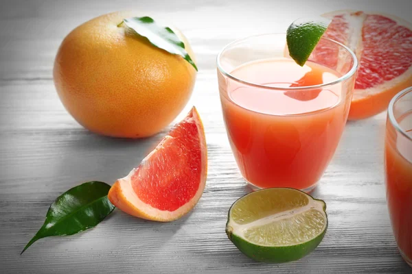 Due bicchieri di succo di agrumi e frutta fresca su sfondo di legno chiaro — Foto Stock