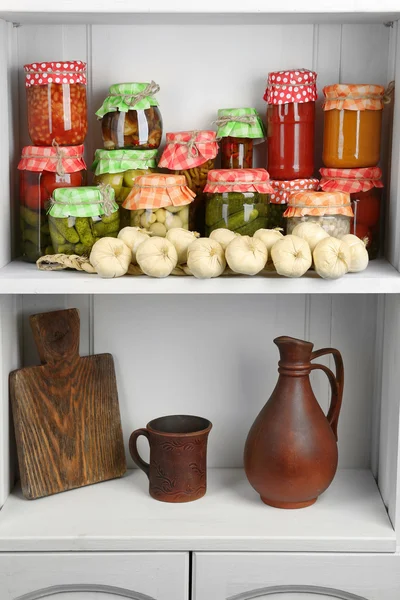 Jars with pickled vegetables and beans, spices, book of recipes and kitchen utensils on shelf — Stock Photo, Image