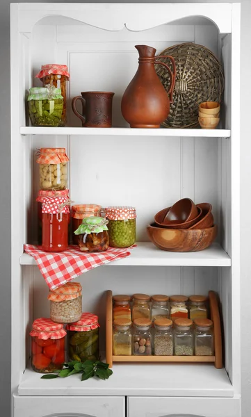 Frascos con verduras y frijoles en escabeche, especias, libro de recetas y utensilios de cocina en estantes de armario —  Fotos de Stock