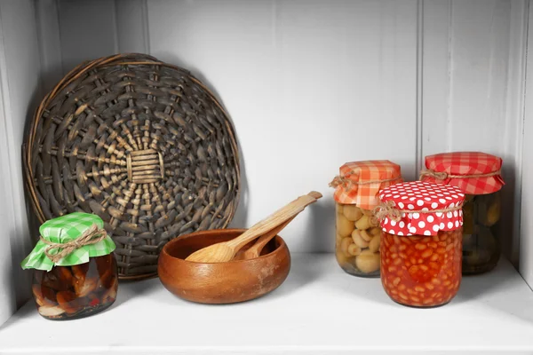 Frascos com legumes em conserva e utensílios de cozinha na prateleira — Fotografia de Stock