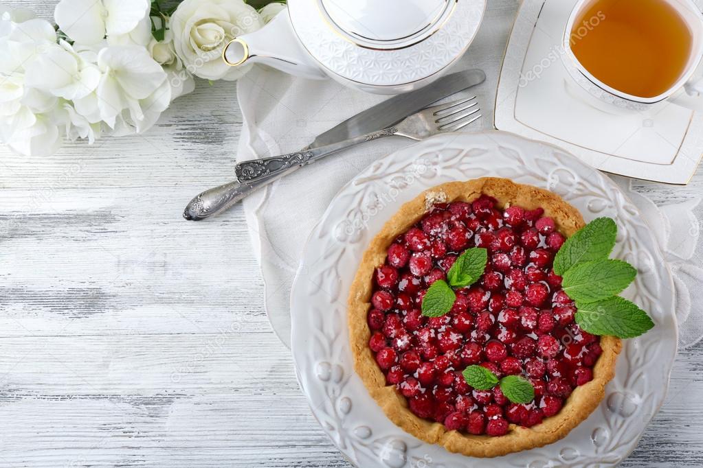 Tart with raspberries and tasty tea, on color  wooden background