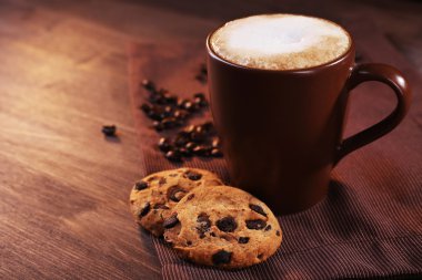 Cup of coffee, cookies with chocolate crumbs and roasted coffee beans on brown napkin on wooden background