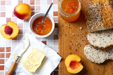 Lezzetli reçel kavanoz ve kase, olgun şeftali ezmesi, taze ekmek ve ahşap tablet mozaik arka plan yakın çekim üzerinde