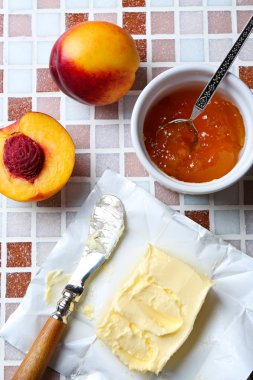 Lezzetli reçel kavanoz ve kase, olgun şeftali, tereyağı ve mozaik arka plan yakın çekim bıçak