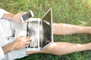 Adam çimenlerin üzerinde oturan dizüstü bilgisayar ile