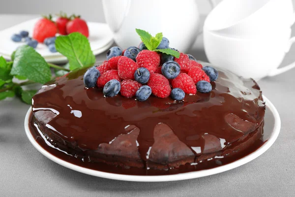 Delicioso bolo de chocolate com bagas de verão em toalha de mesa cinza, close-up — Fotografia de Stock