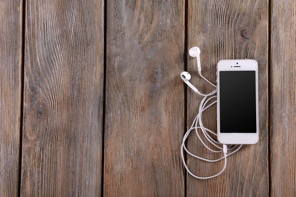 Celular branco com fones de ouvido em fundo de madeira — Fotografia de Stock