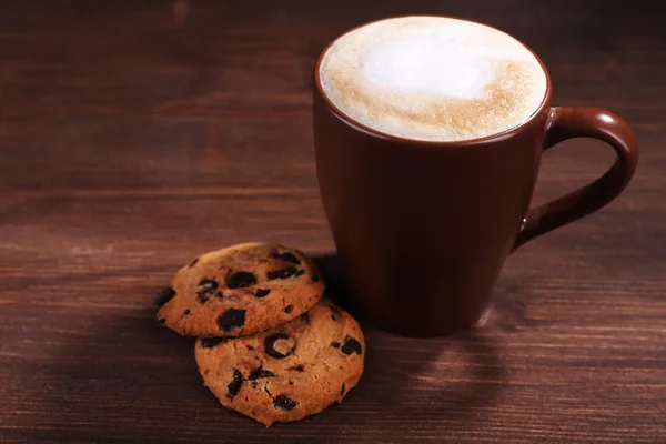 Φλιτζάνι καφέ με αφρό γάλακτος και τα cookies σε φόντο ξύλινη — Φωτογραφία Αρχείου