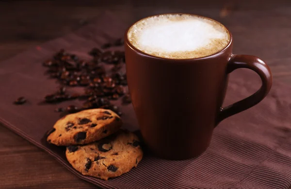 Xícara de café, biscoitos com migalhas de chocolate e grãos de café torrados em guardanapo marrom em fundo de madeira — Fotografia de Stock
