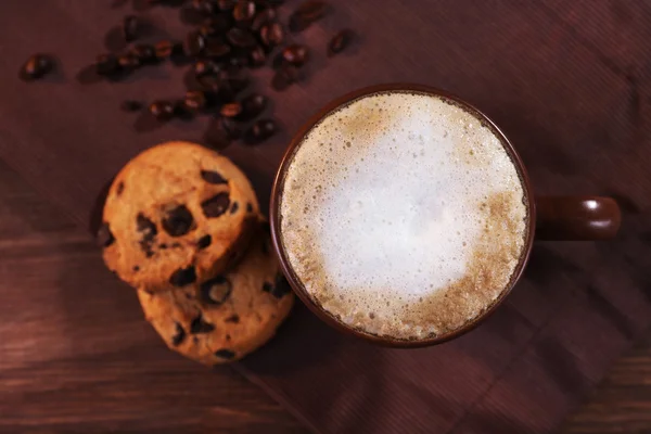 Tasse Kaffee, Kekse mit Schokoladenbröseln und gerösteten Kaffeebohnen auf brauner Serviette auf Holzgrund — Stockfoto