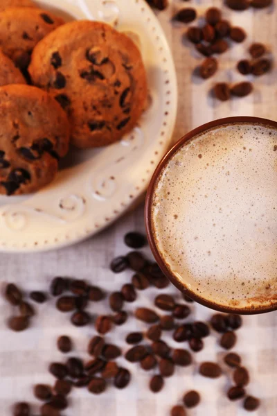 Чашка кофе, вкусное печенье и кофейные зерна, разбросанные по салфетке, вид сверху — стоковое фото