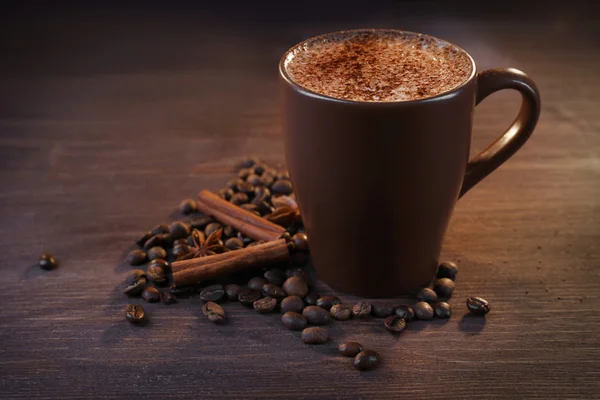 Lekkere warme koffie met geroosterde bonen en kaneel rond op houten achtergrond — Stockfoto