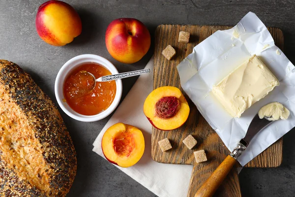 Confiture savoureuse dans le bol, pêches mûres, beurre, craquelins et pain frais sur tablette en bois close-up — Photo