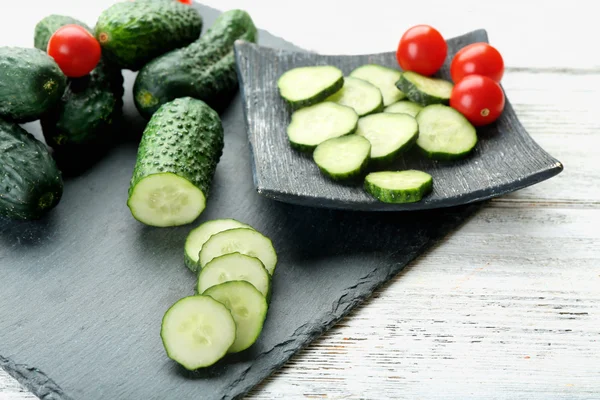 Sliced cucumbers with tomatoes on black plank on wooden background — Stock Photo, Image