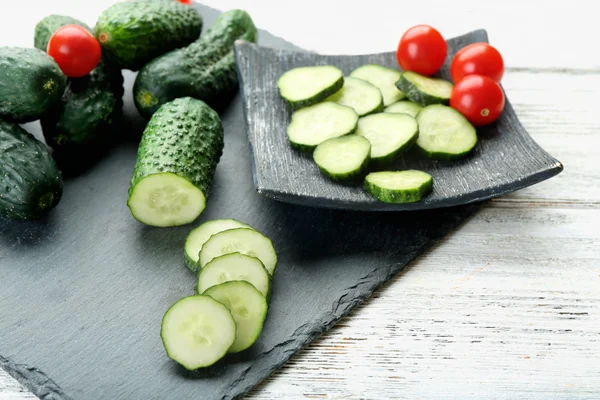 Pepinos en rodajas con tomates sobre tabla negra sobre fondo de madera —  Fotos de Stock