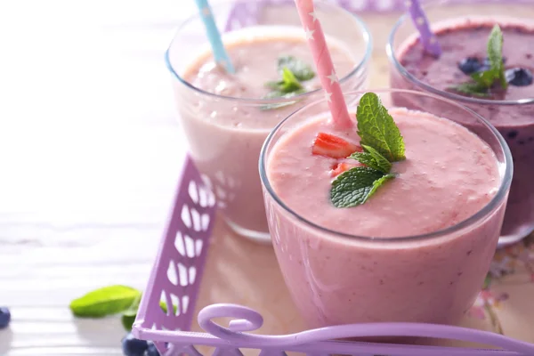 Savoureux yaourt aux fraises, bleuets et lait sur serveur sur fond bois clair, gros plan — Photo