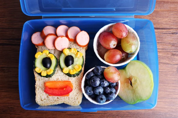 Creative sandwich with fruits in lunchbox on wooden background — Stock Photo, Image