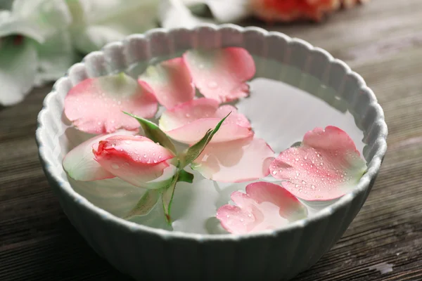 Нежная розовая роза и лепестки в чаше с водой на деревянном фоне — стоковое фото