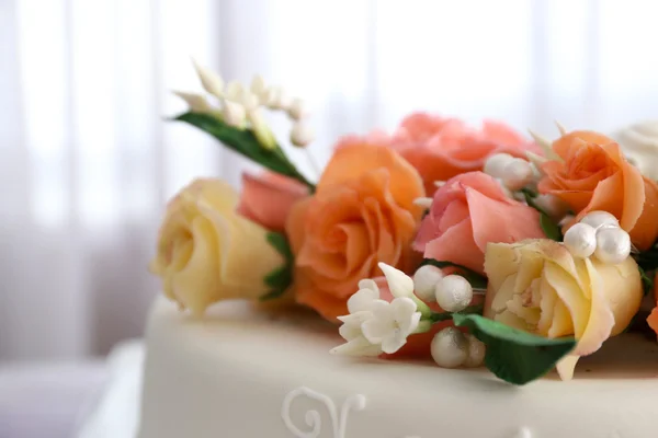 Beautiful wedding cake decorated with flowers on table in the room, close up