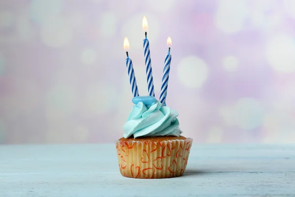 Sweet cupcake with candles on blue wooden table against blurred background