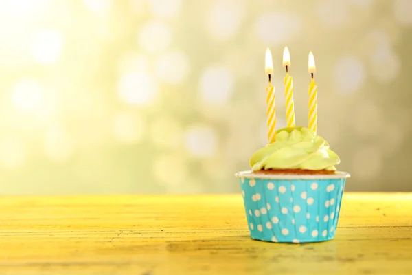 Smakelijke cupcake met kaarsen op gele houten tafel tegen ongericht achtergrond — Stockfoto