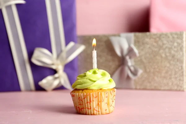Gustoso cupcake con candela sul tavolo rosa contro colorate scatole presenti sfondo — Foto Stock