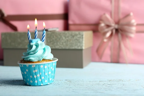 Pembe mevcut kutuları karşı mavi ahşap masa mum ile tatlı kek — Stok fotoğraf