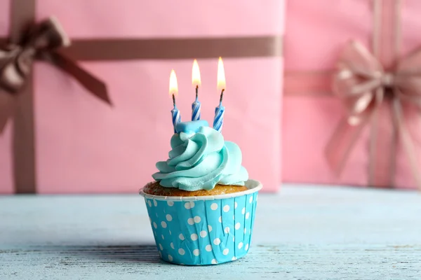 ピンクのプレゼント ボックスに対して青い木製テーブルの上の蝋燭と甘いカップケーキ — ストック写真