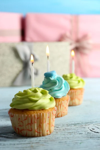 Delicious cupcakes with candles on violet table against wooden background — Stock Photo, Image