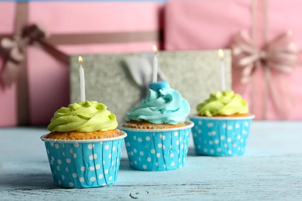 Delicious cupcakes with candles on violet table against wooden background — Stock Photo, Image