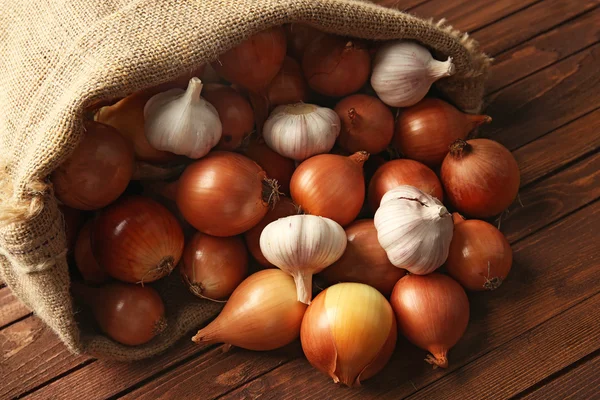 Saco disperso con cebollas frescas y ajo sobre fondo de madera — Foto de Stock