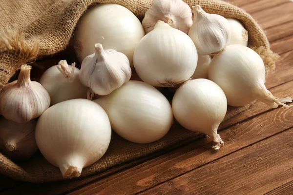 Sacchetto sparso con cipolle e aglio su fondo di legno — Foto Stock