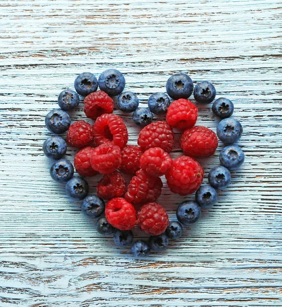 Heart shaped raspberries and blueberries on old wooden background — Stock Photo, Image