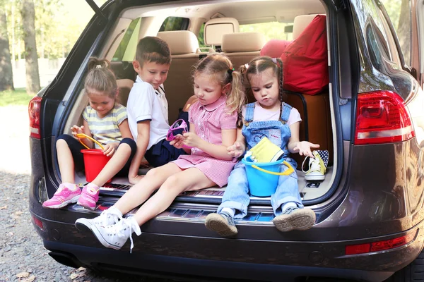 Três meninas bonitas e menino sentar em um carro tronco e rindo — Fotografia de Stock