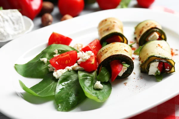 Zucchini rolls with cheese, bell peppers and arugula on plate, close-up, on table background — Stock Photo, Image