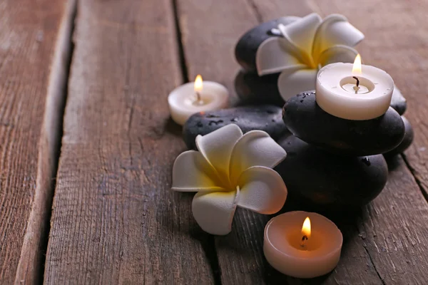 Relaxing composition with exotic fragipani flower, pebbles and candles on wooden background — Stock Photo, Image