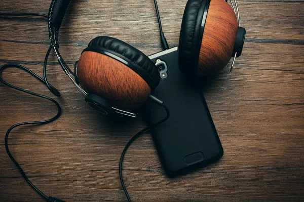 Auriculares y smartphone sobre fondo de madera marrón —  Fotos de Stock