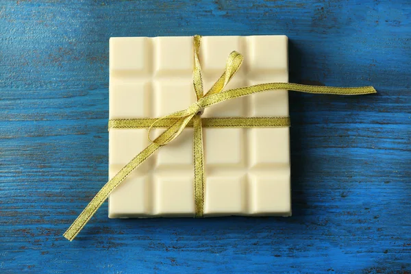 Weiße Schokolade mit bunten Schleifen auf farbigem Holzhintergrund — Stockfoto