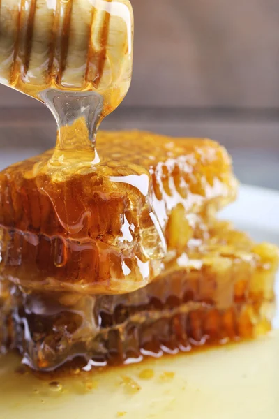 Mel pingando em favos de mel na placa no fundo de madeira — Fotografia de Stock