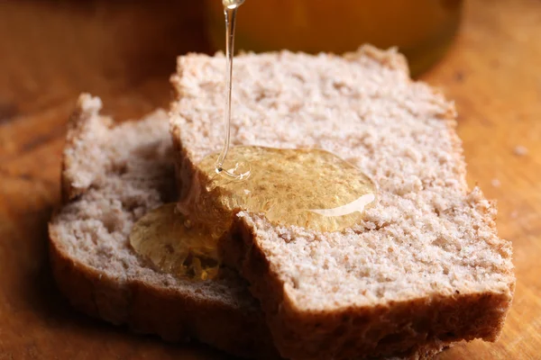 Honey dripping on fresh bread on wooden background