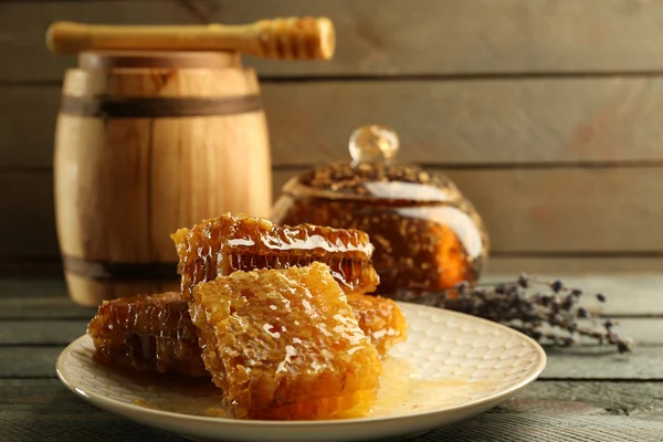 Favi su piatto, pentola con miele e botte di legno su fondo di legno — Foto Stock
