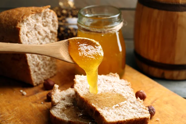 Honey dripping on fresh bread on wooden background — Stock Photo, Image